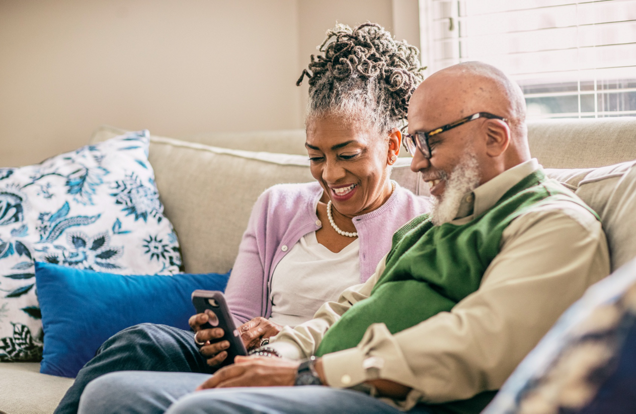 Older couple sitting on a sofa looking at somehting on their phone.